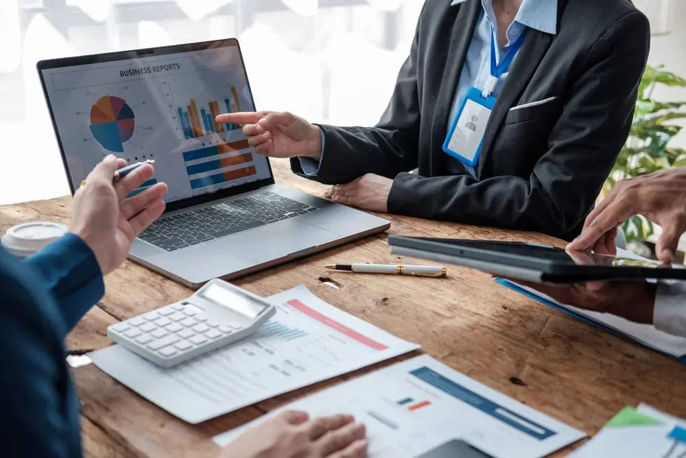 Close-up of business professionals discussing data charts on a laptop screen, illustrating procurement consulting services.